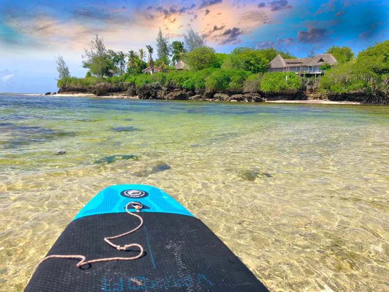 Paddleboarding over clear shallow water toward The Rock and Sea