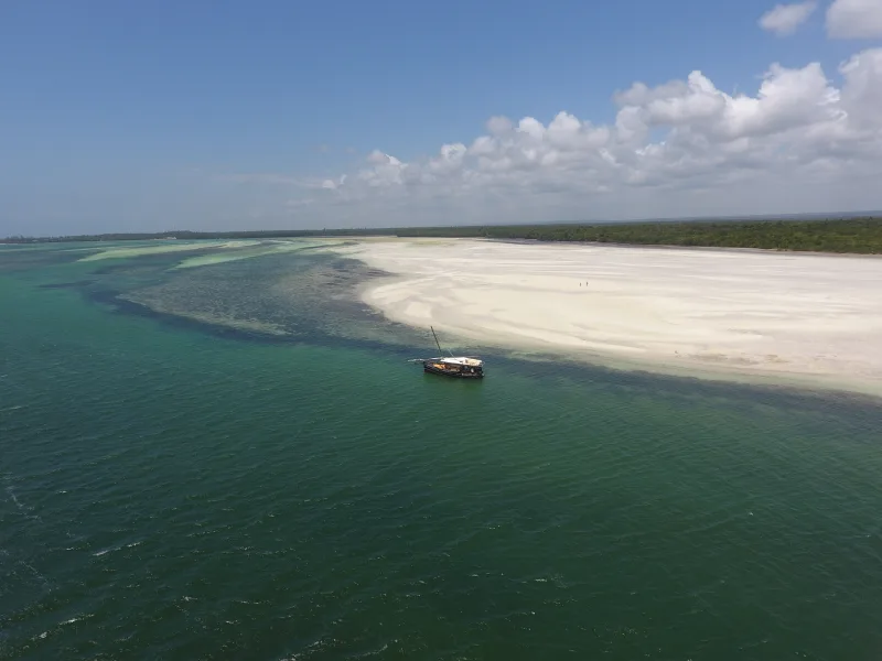 A white sandbank curving into the shallows of Mida Creek, the dhow moored offshore