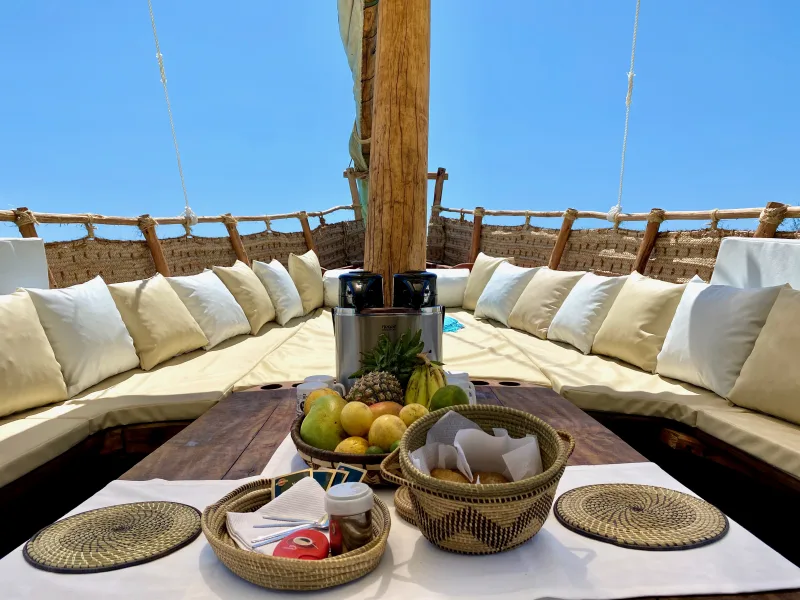 The shaded deck laid for lunch, with fresh fruit and cushioned seating around the mast